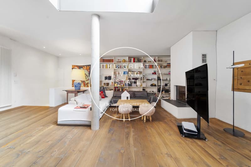 Modern living room with hardwood floors, white walls, a large bookshelf, a fireplace, a white sofa, a coffee table, a table lamp, a table with a blue vase, and a mounted TV.