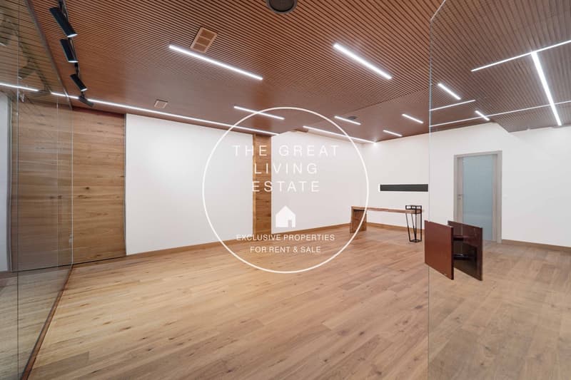 large open space, hardwood floors, glass walls, ceiling lighting, white walls, wooden door, table, no furniture