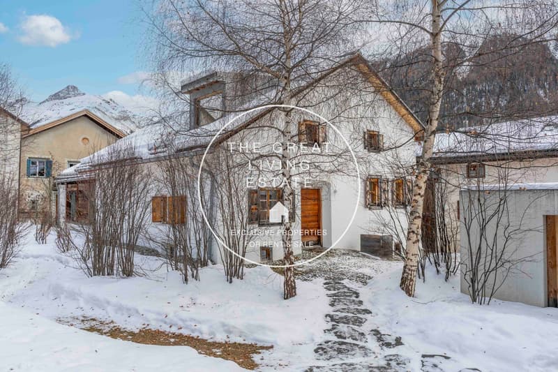 Snow-covered exterior, rustic design, wooden doors, snow-covered roofs, surrounded by trees, mountains in the background.