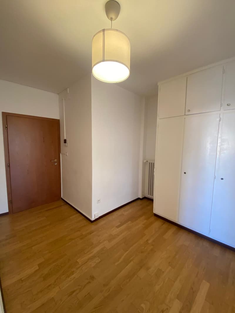 empty room, hardwood floor, white walls, a door, built-in cabinets, a light fixture, power outlet, radiator