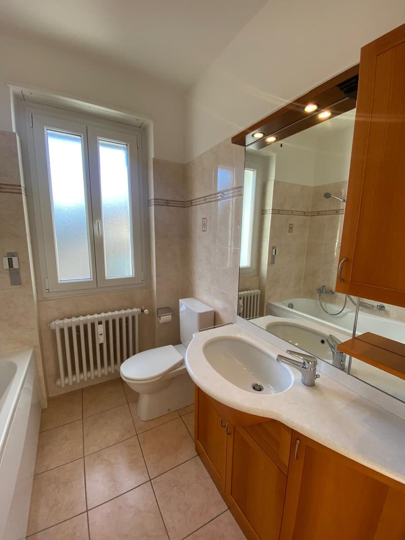 Tiled floor, white bathtub, white toilet, sink, large mirror, wooden cabinets, window