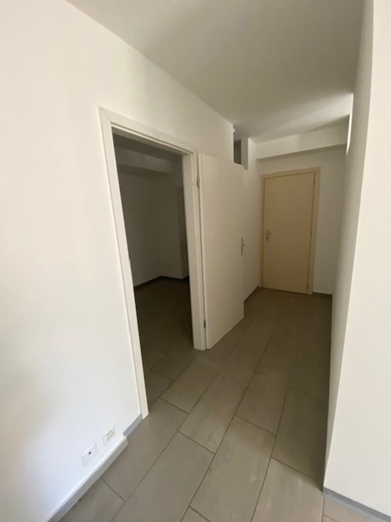 The image shows a hallway with white walls and a tiled floor. There is a doorway visible leading to another room.