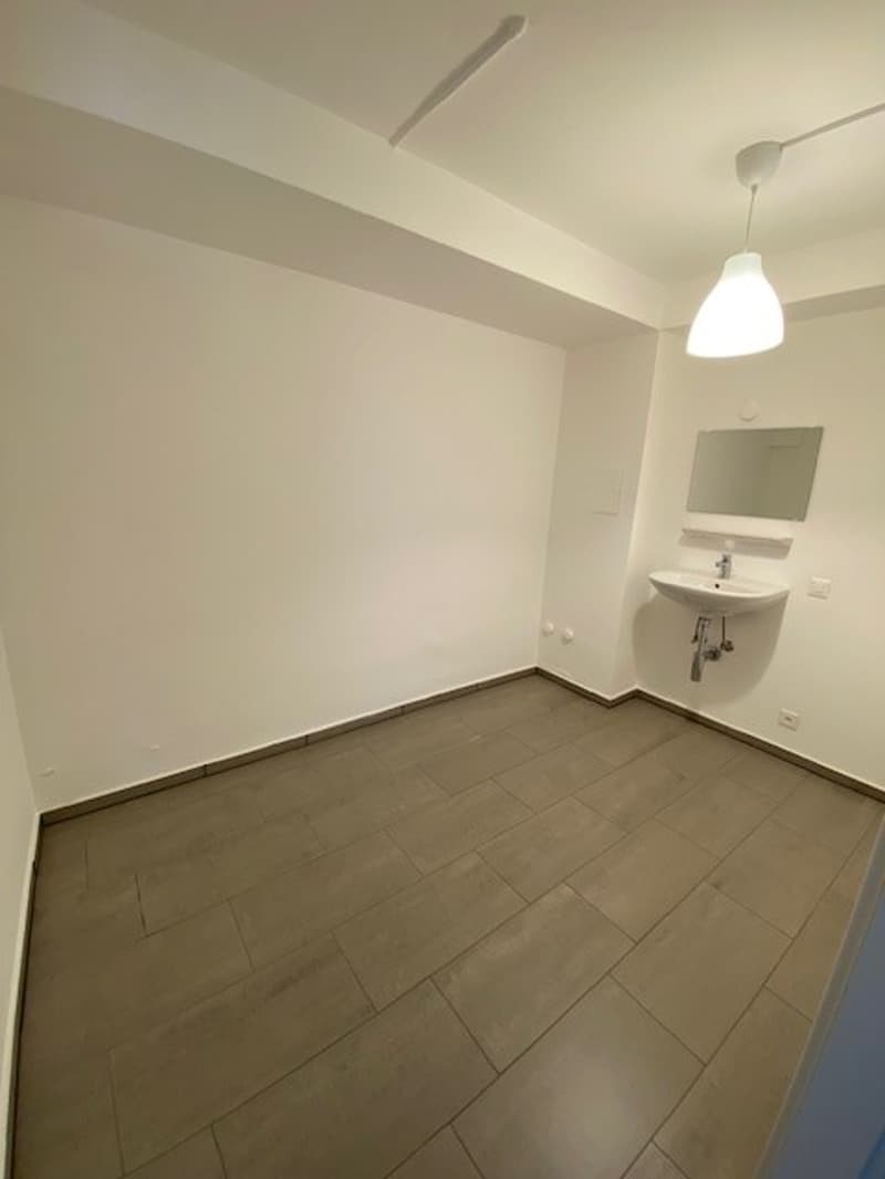 Empty room with white walls, gray tile flooring, and a light fixture on the ceiling.