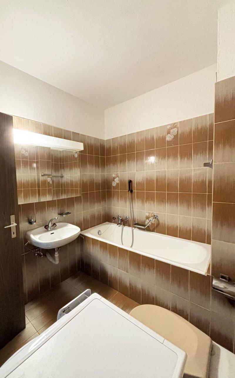 Bathroom with bathtub, sink, mirror, and toilet with shower attachment.