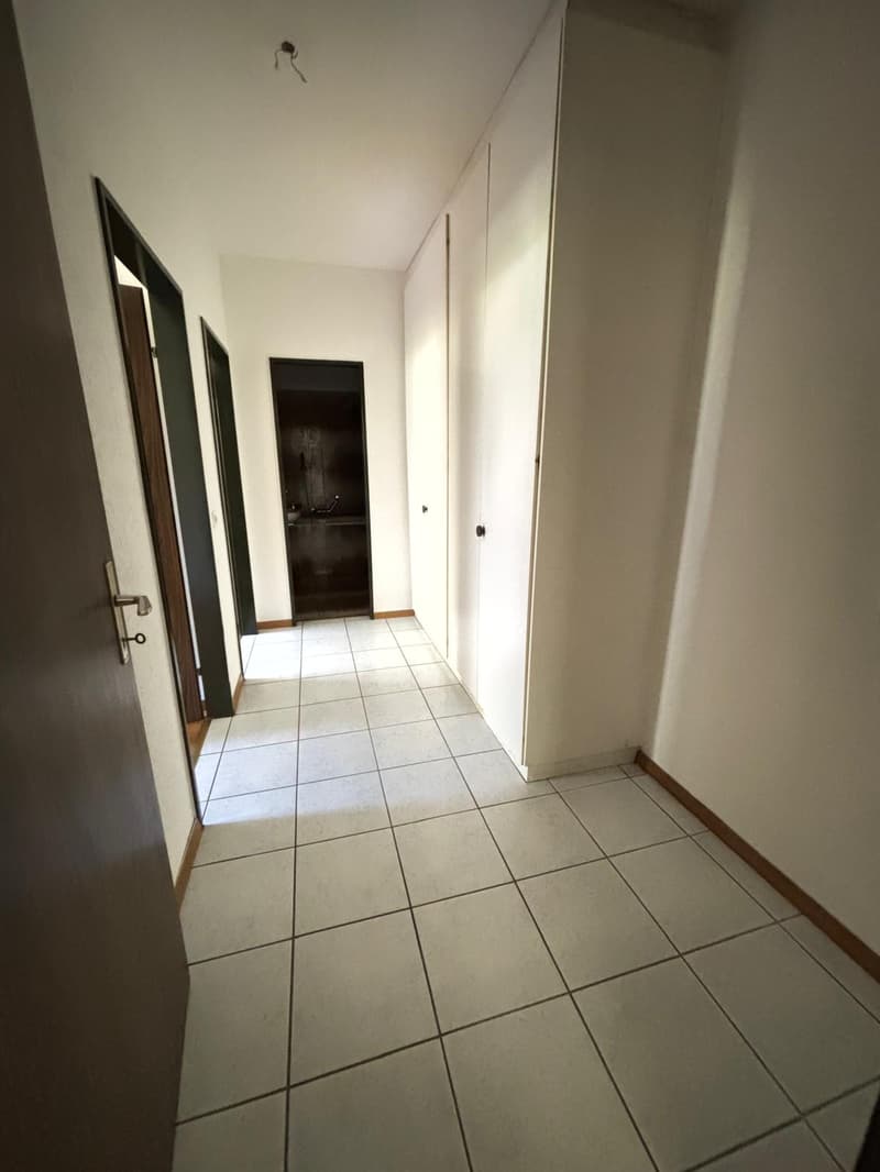 Corridor with white tiles, white walls, and open doors leading to rooms