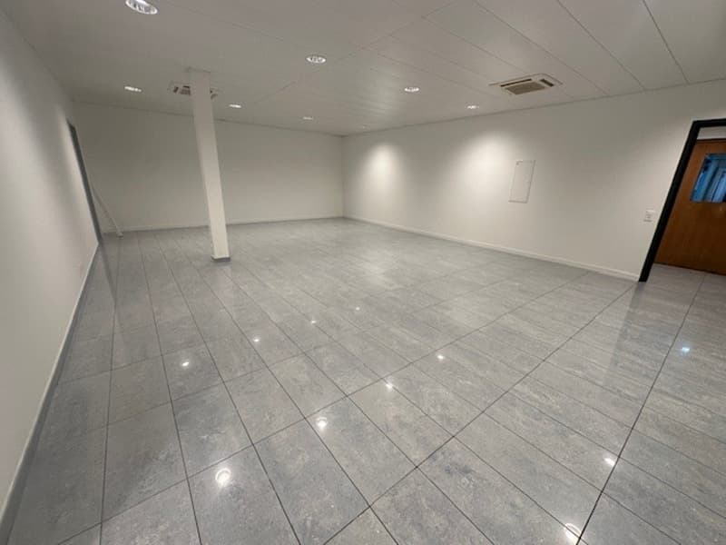 white walls, gray floor tiles, column in the middle, white ceiling, lights on the ceiling, empty room