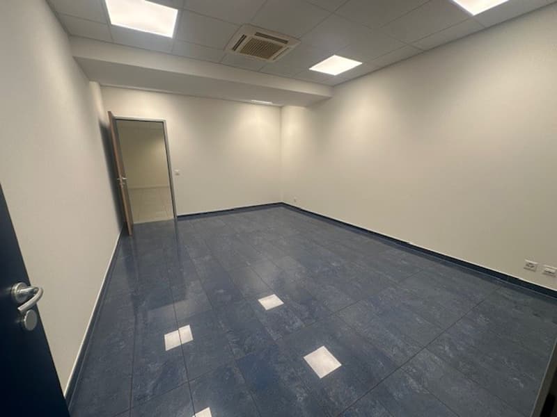 empty office room with blue tiles, open door, white walls, ceiling lamps