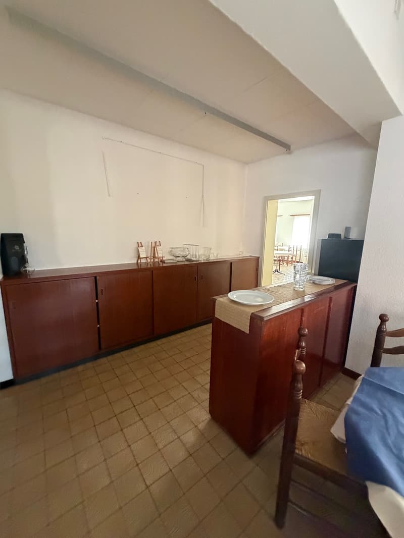a kitchen with white wall and tile flooring, wooden cabinets, and a small dining area