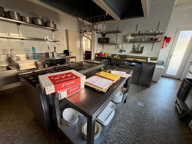 Stainless steel appliances, industrial oven, metal shelves, open floor plan, clean surface, pots, pans, utensils, microwave, refrigerator, kitchen tools
