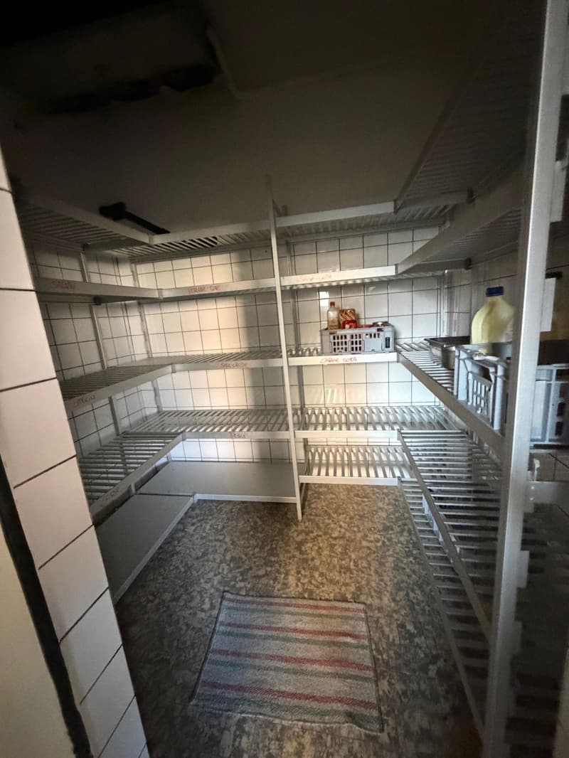 Empty pantry with tiled walls and shelves, two plastic baskets on the top shelf, and a rug on the floor.