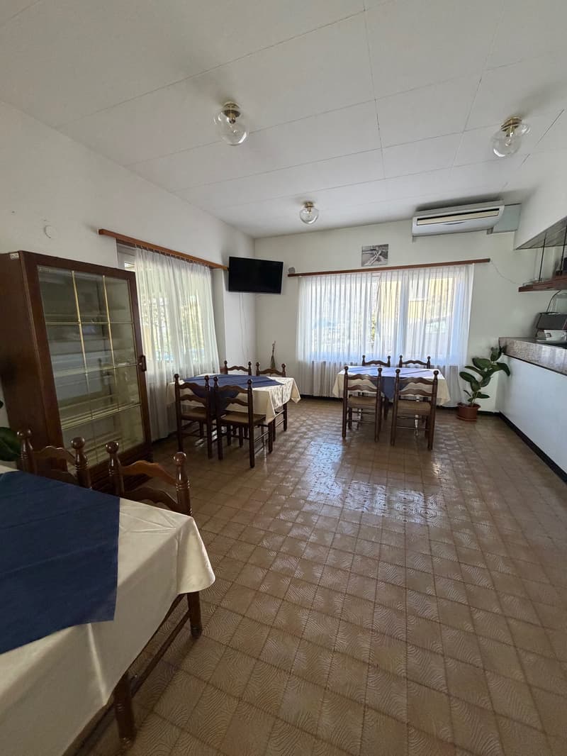 empty dining room with wooden flooring, table and chairs, mounted tv, glass cabinet, and a plant