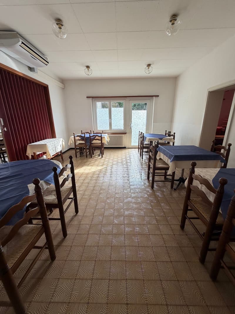Wooden dining chairs, tables with tablecloths, tiled flooring, red curtain, windows with glass, door, white air conditioner