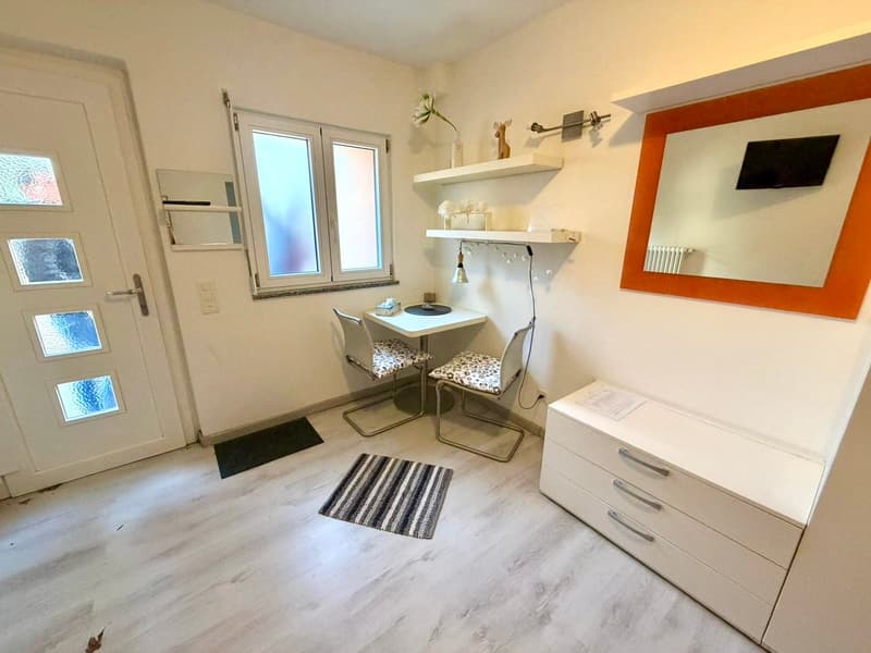 small room with desk, chairs, shelves, mirror, and a white cabinet