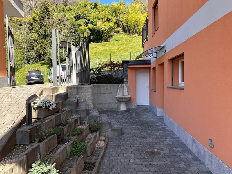 orange building, raised ground floor, paved walkway, steps, fountain, car parked