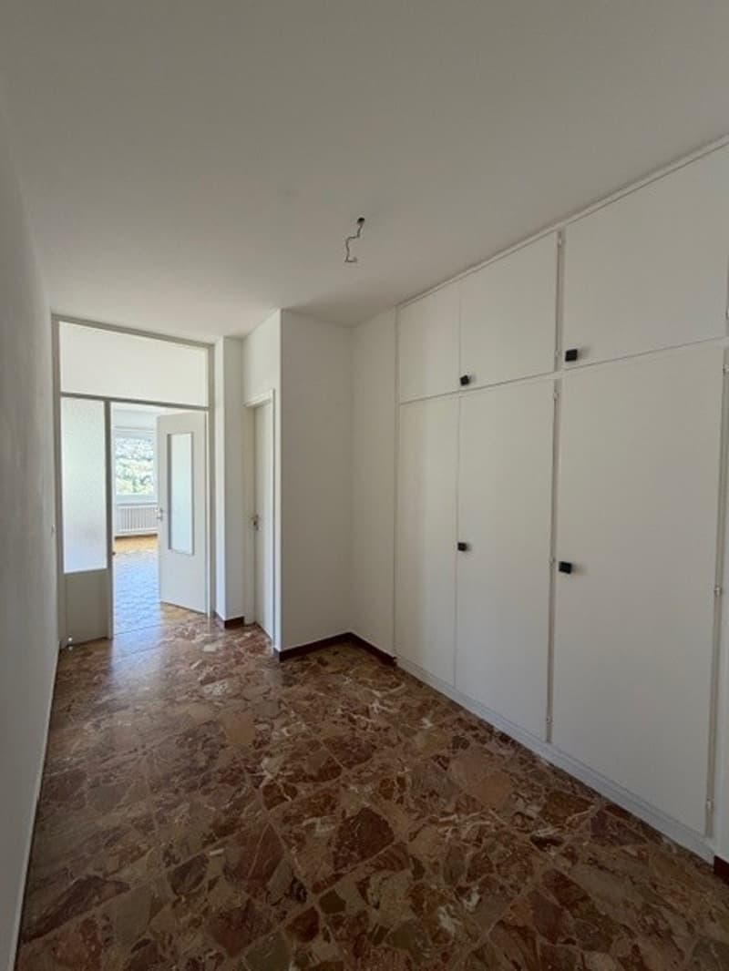 Empty room with white walls, brown marble floor, white doors, and white cabinets