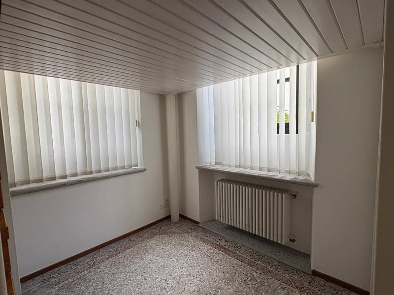 An empty room with two windows, white walls, white blinds, radiators, and white tile flooring.