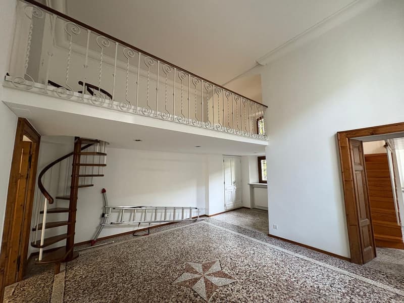 A room with white walls, wooden floor, spiral staircase, balcony with wrought iron railing, white ceiling, and a large star-patterned tile floor.