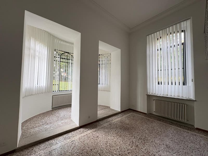 large room with arched doorways, stone floor, vertical blinds on windows, white walls, radiators