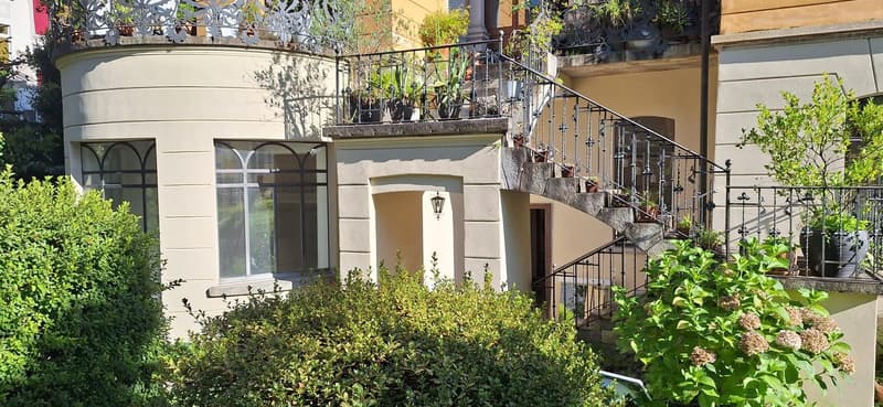 white stucco, arched windows, metal railing, spiral staircase, plants, lamp