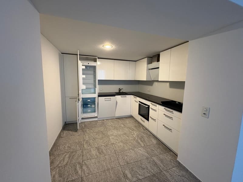 modern white kitchen with tiled floor, open refrigerator, built-in oven and sink, black countertops, white cabinets, and a power outlet on the wall
