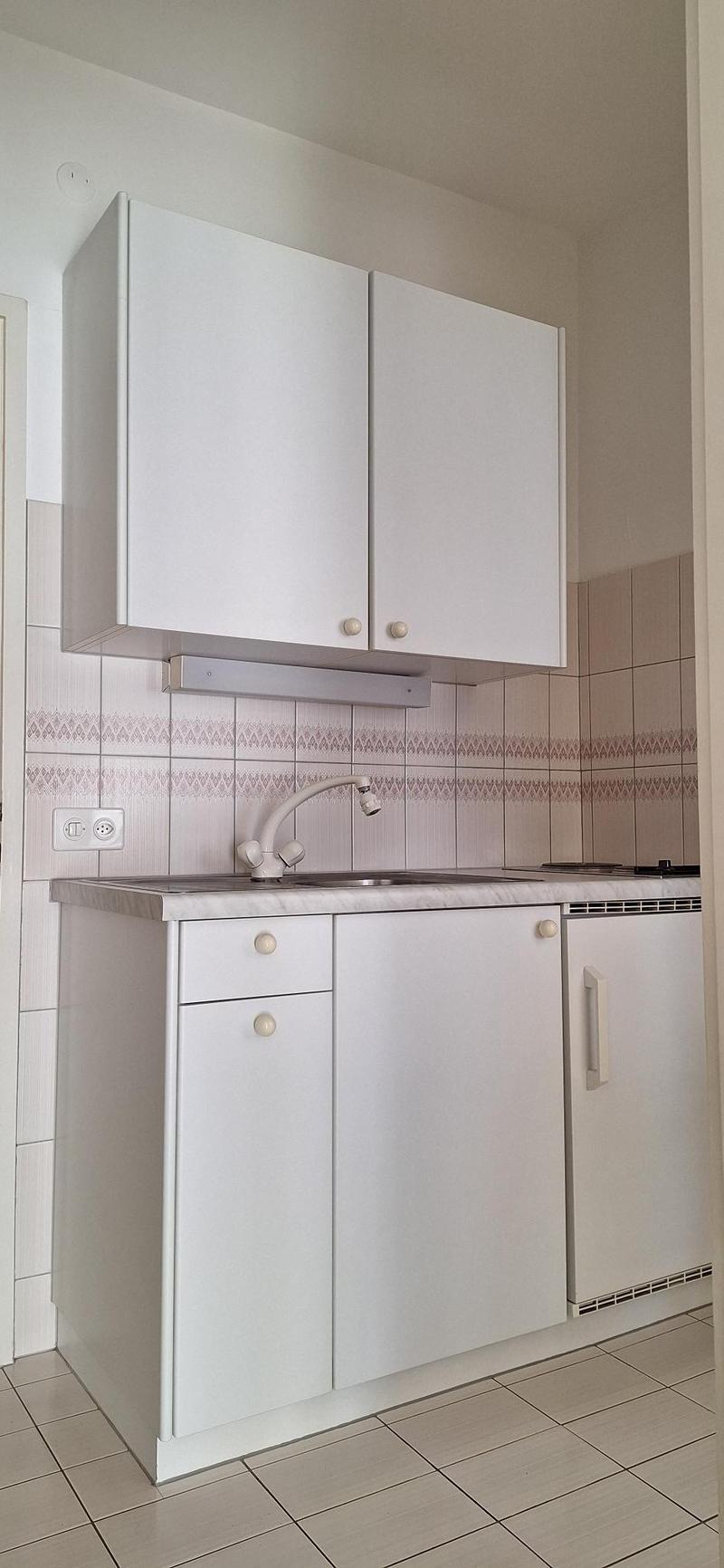 a modern kitchen with white cabinets, white countertops, integrated dishwasher, washing machine, and gas stove. It has decorative tiles on the walls, and a sink with a faucet.