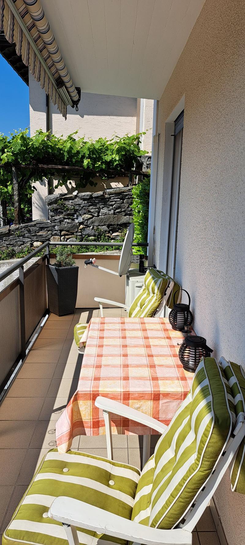 tiled balcony, green striped chairs, table with checkered tablecloth, plants, table lamps, shade