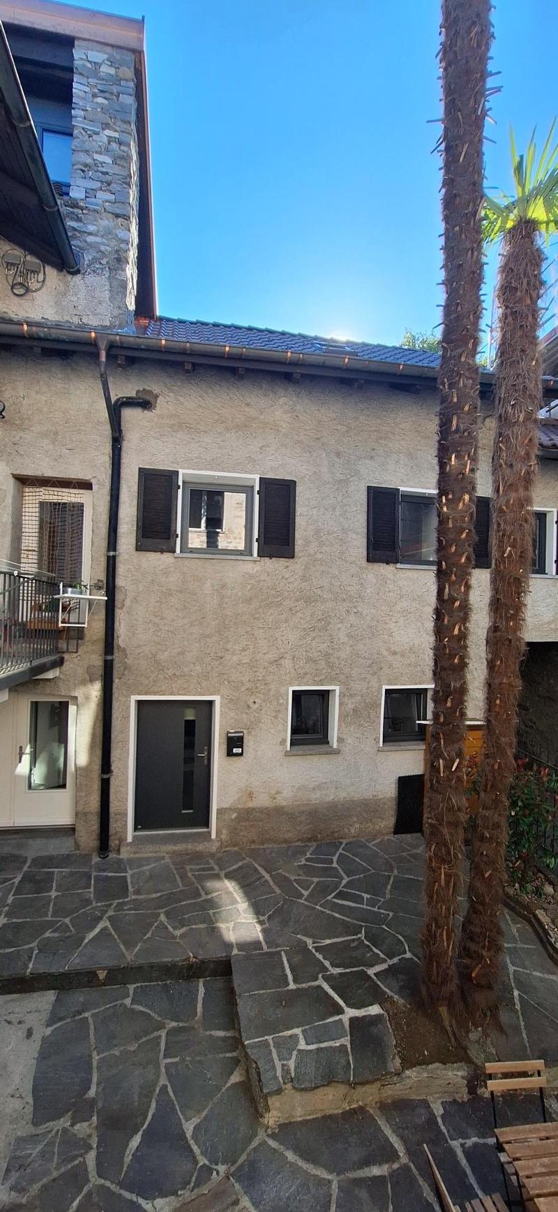 Stone building, multiple windows, black shutters, black door, stone pavement, balcony, palm trees