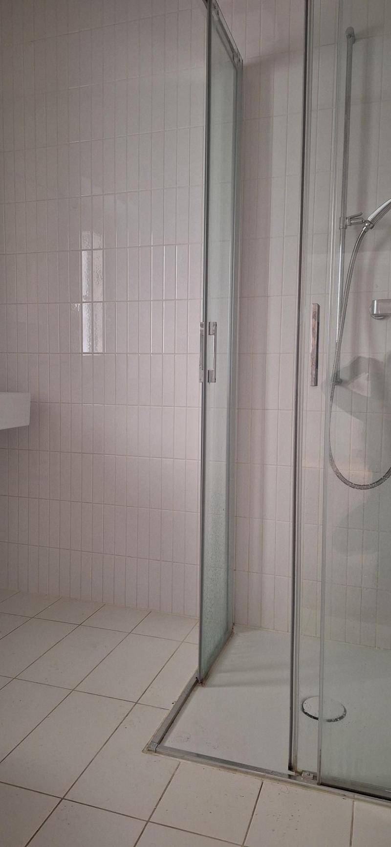white tiled walls, white tiled floor, glass shower enclosure, shower head, drain
