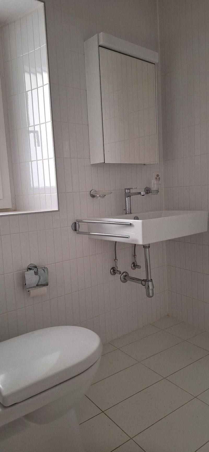 Bathroom with white tiles, white sink, silver faucet, white toilet, mirror, and a window