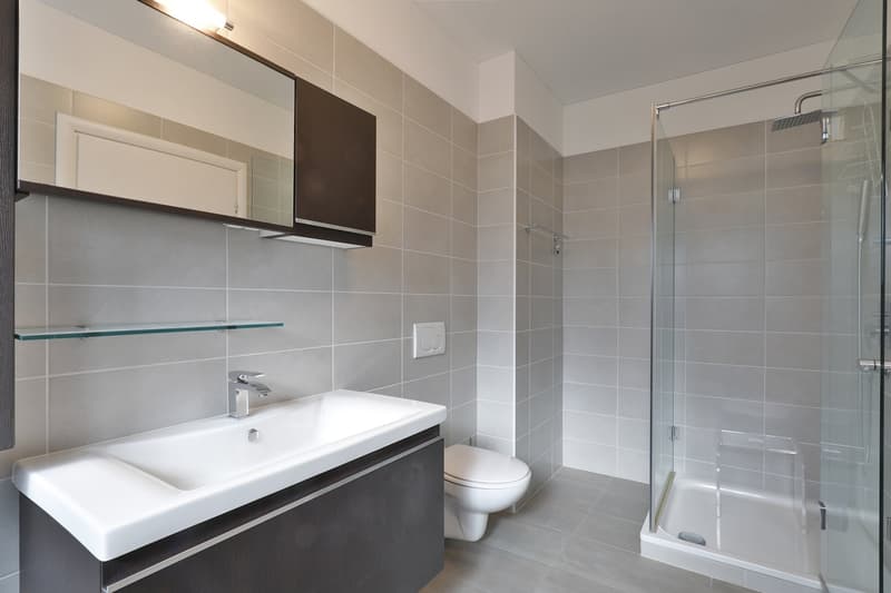 modern bathroom with a white sink, gray tiles, a mirror, and a toilet in the corner