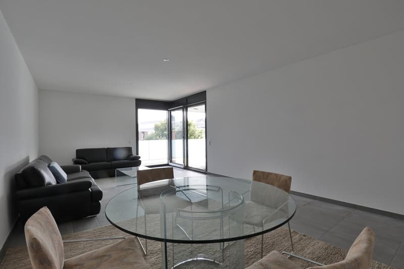 Open living room with glass table and glass doors, black leather sofa, large sliding doors with balcony access