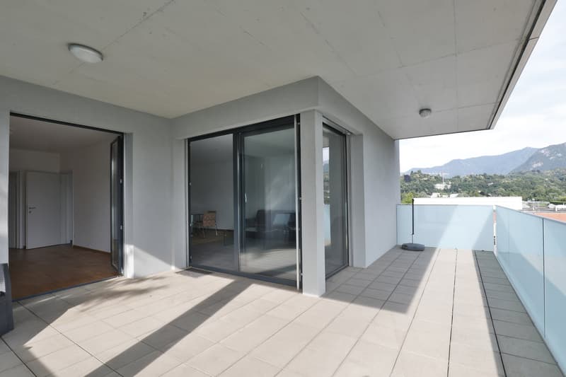 Spacious apartment with large windows, sliding glass doors leading to a balcony or terrace, hardwood floors, and a view of the surrounding mountains.