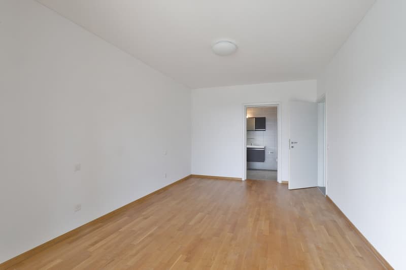 Empty room with white walls, hardwood flooring, and a doorway leading to another room.