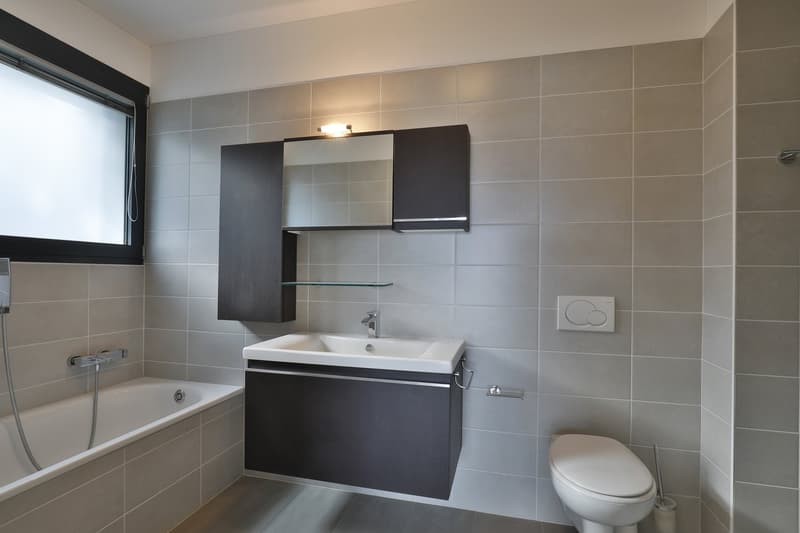 modern and minimalist bathroom with bathtub, sink, mirror, and toilet