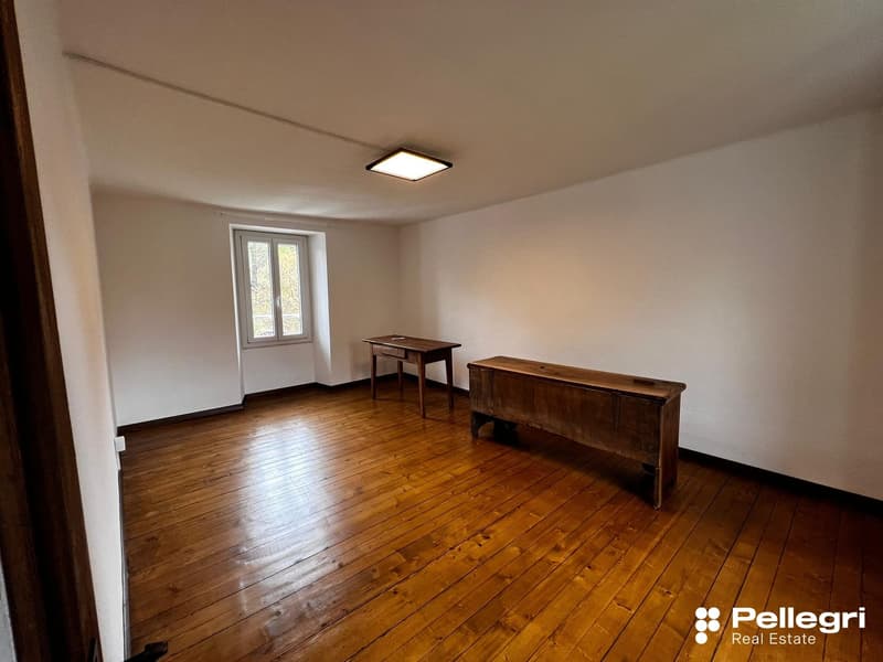 Empty room with hardwood floors, white walls, and a window. The room contains a wooden desk and a wooden bench.