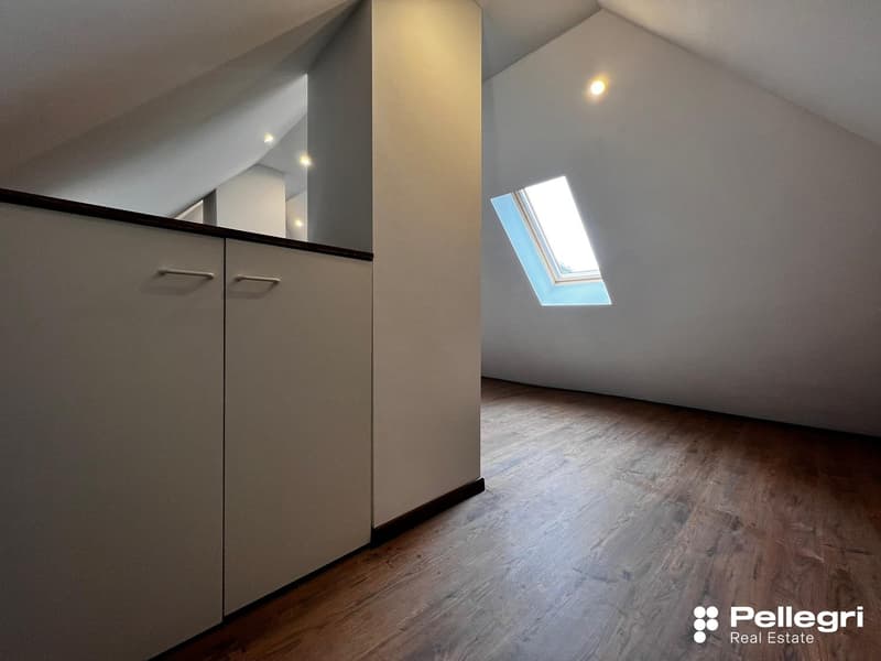 Spacious attic bedroom with hardwood flooring, built-in cabinets, and a skylight providing natural light