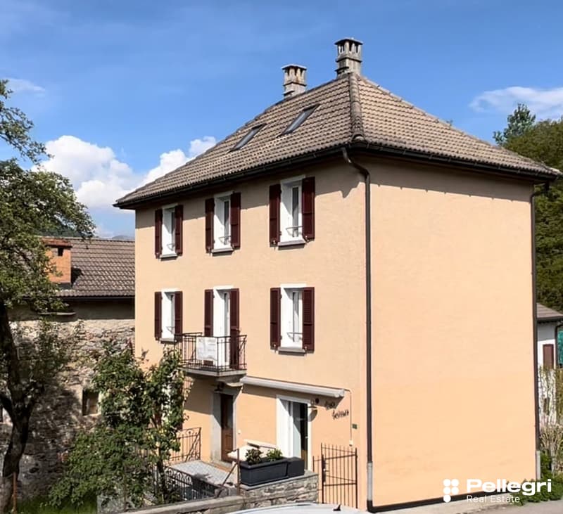 2 story house, yellow exterior, red tile roof, white windows with shutters, balcony, garden