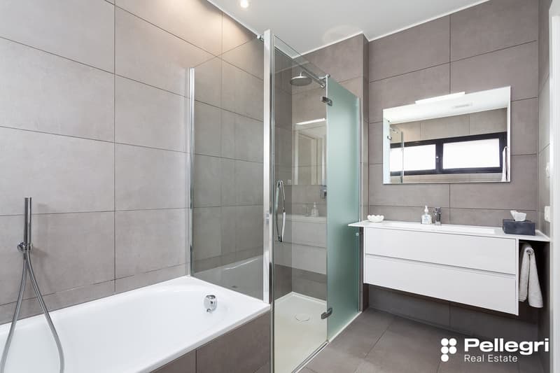 Large bathroom with gray tile walls, glass shower enclosure, freestanding bathtub, and a white vanity with drawers