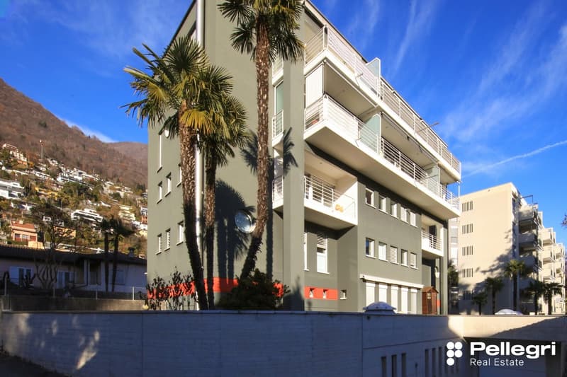 4 story building, gray exterior, red stripe, white windows, balconies, trees, hillside in background