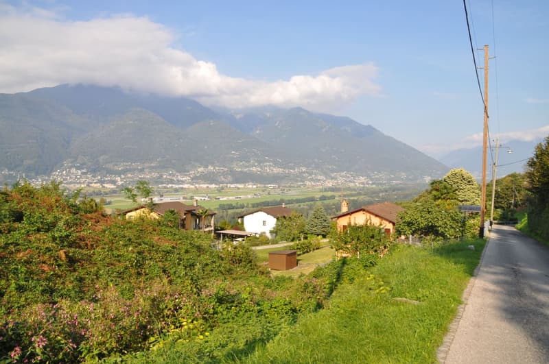 Mountainside residential area with houses, green landscape, distant city, pathway, electricity poles