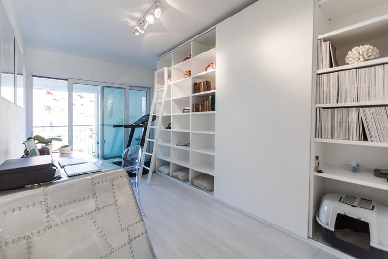 modern office room with white shelves, treadmill, desk, chair, books, cat litter box