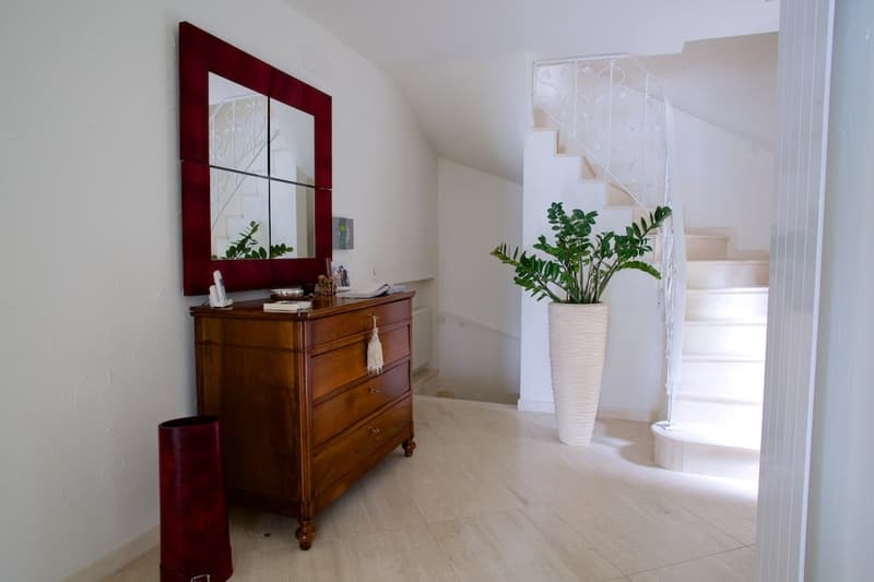 Spacious entryway with hardwood floors, a large wooden dresser with a decorative mirror, and a potted plant. The staircase is visible in the background.