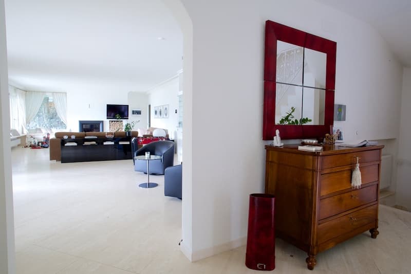 Open concept living room with white walls, hardwood floors, a large TV stand, a red framed mirror, and a wooden dresser with decorative items.