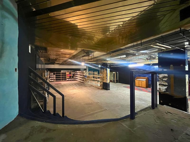 Large open space, wooden shelves, wooden pallets, blue wall, grey flooring, stairs on left, cabinet on the right