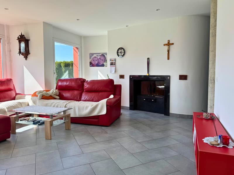 Spacious living room with red leather sofa, coffee table, wall-mounted TV, religious decor, and tiled flooring