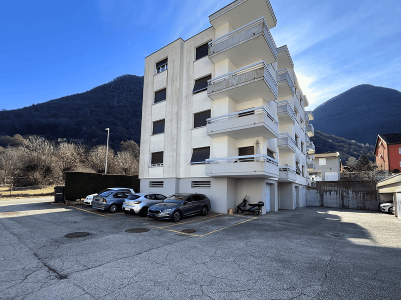 3 story apartment building, white exterior, multiple balconies, 4 cars parked in front, street lamp