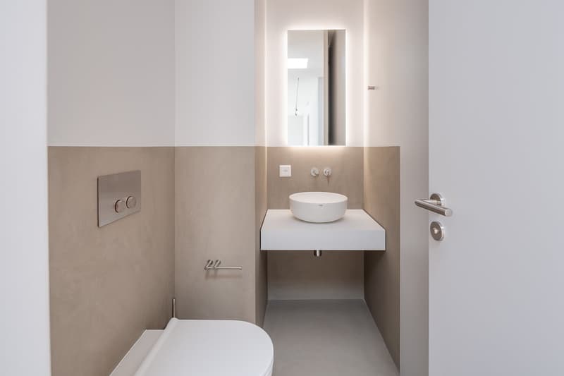 modern bathroom with white toilet, white sink, mirror, and beige walls