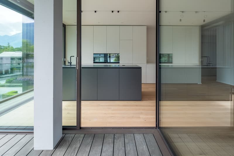 modern kitchen with island, large windows, wooden floor, sliding glass doors to balcony