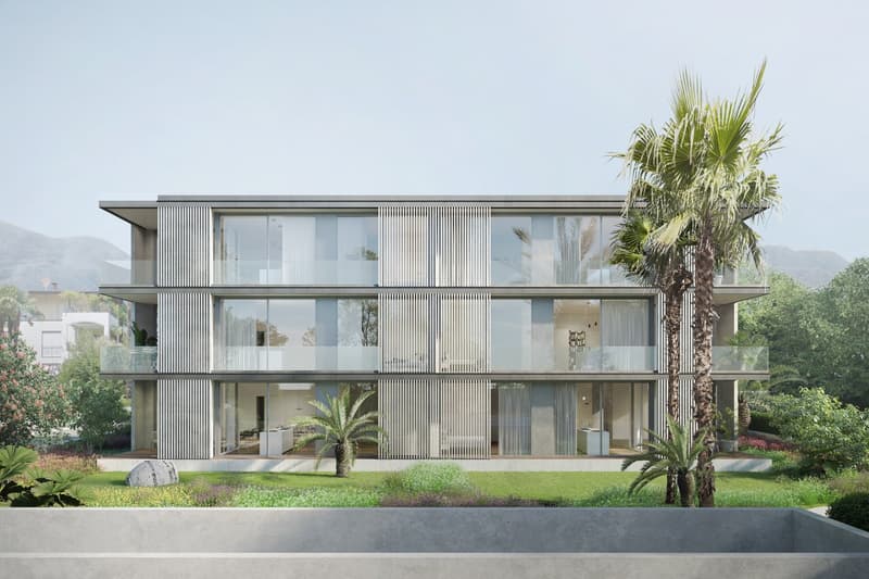 Modern apartment building with glass walls, balconies, and a garden