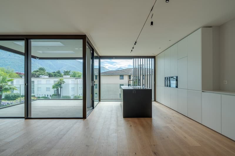 modern kitchen with large windows, wooden floor, island with sink, white cabinets, balcony